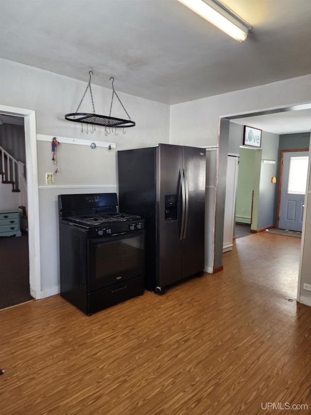 kitchen with baseboards, stainless steel fridge with ice dispenser, wood finished floors, black range with gas stovetop, and a baseboard heating unit