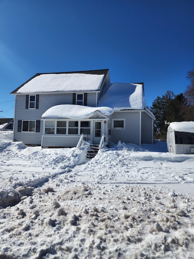 snow covered back of property with a sunroom, an outdoor structure, and a storage shed