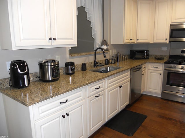 kitchen with light stone counters, dark wood-style flooring, a sink, white cabinets, and appliances with stainless steel finishes