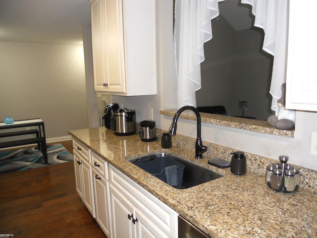 kitchen featuring light stone counters, a sink, baseboards, white cabinets, and dark wood finished floors