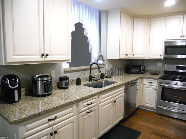 kitchen with light stone counters, dark wood-style floors, stainless steel appliances, white cabinetry, and a sink