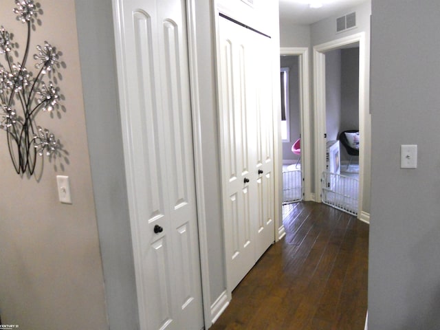 hallway with baseboards, visible vents, and dark wood-type flooring