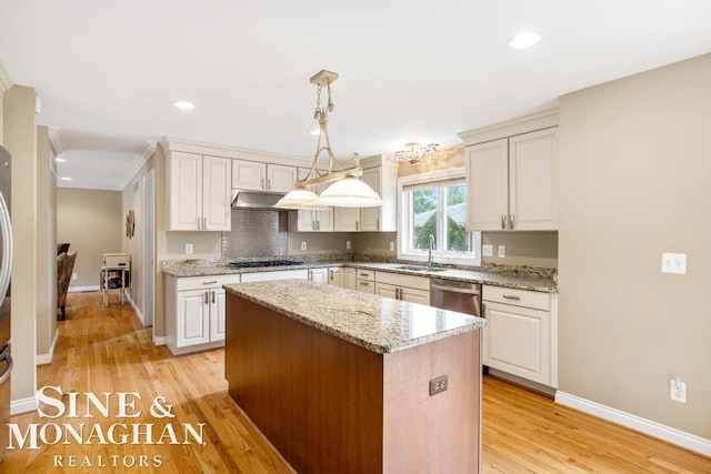 kitchen with appliances with stainless steel finishes, a center island, light stone countertops, light wood-style floors, and a sink