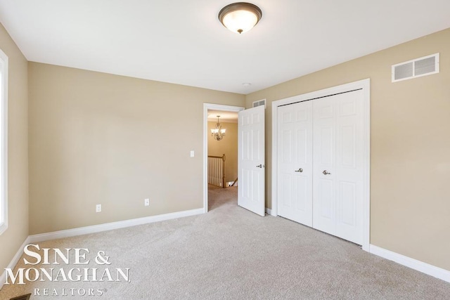 unfurnished bedroom with a notable chandelier, a closet, visible vents, carpet flooring, and baseboards