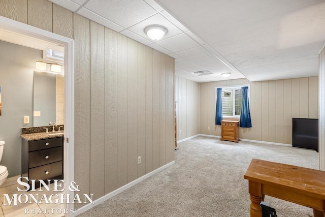 interior space with carpet, visible vents, wood walls, a drop ceiling, and baseboards