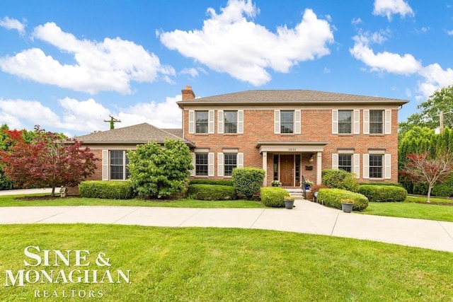 colonial home featuring brick siding, a chimney, and a front lawn