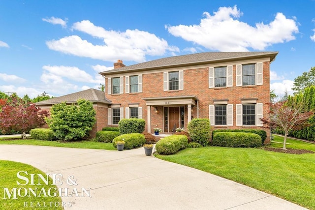 colonial home featuring concrete driveway, brick siding, a chimney, and a front yard