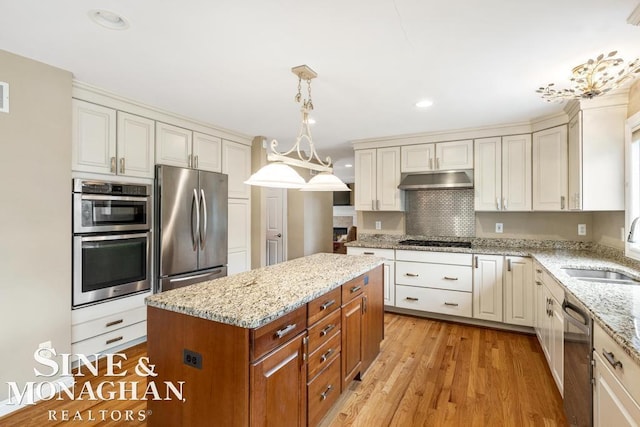 kitchen with light wood-style flooring, appliances with stainless steel finishes, a sink, light stone countertops, and under cabinet range hood