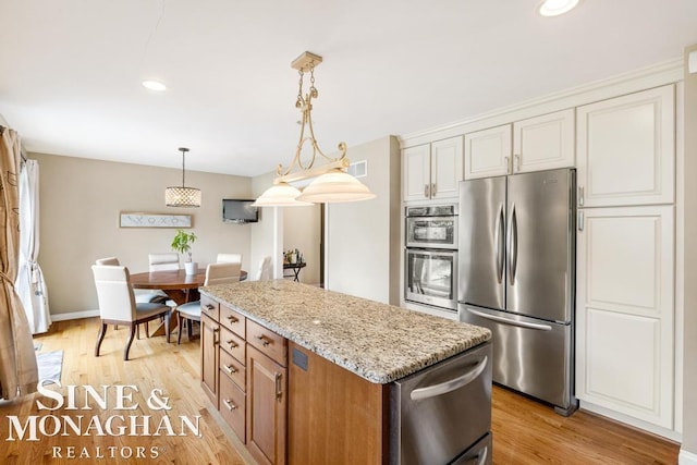 kitchen with appliances with stainless steel finishes, light wood-type flooring, a kitchen island, and light stone counters