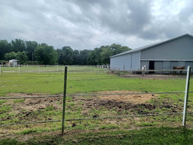 view of yard featuring a rural view, fence, a pole building, and an outdoor structure