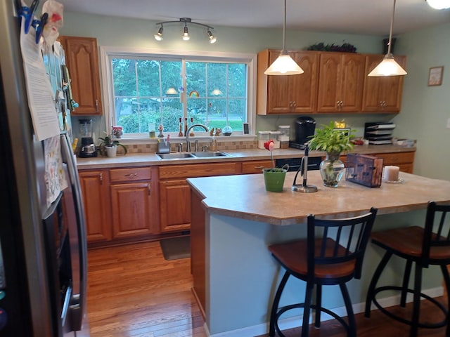 kitchen featuring brown cabinets, freestanding refrigerator, light wood-style floors, a kitchen bar, and a sink