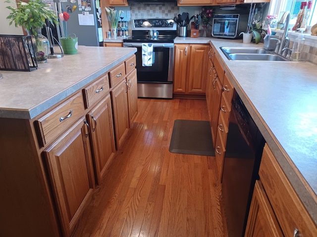 kitchen with stainless steel appliances, a sink, light countertops, light wood finished floors, and brown cabinetry