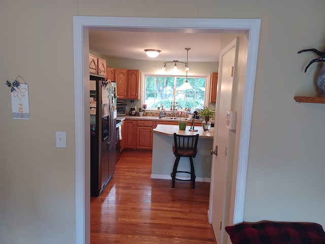 kitchen featuring stainless steel fridge, a kitchen breakfast bar, wood finished floors, light countertops, and a sink