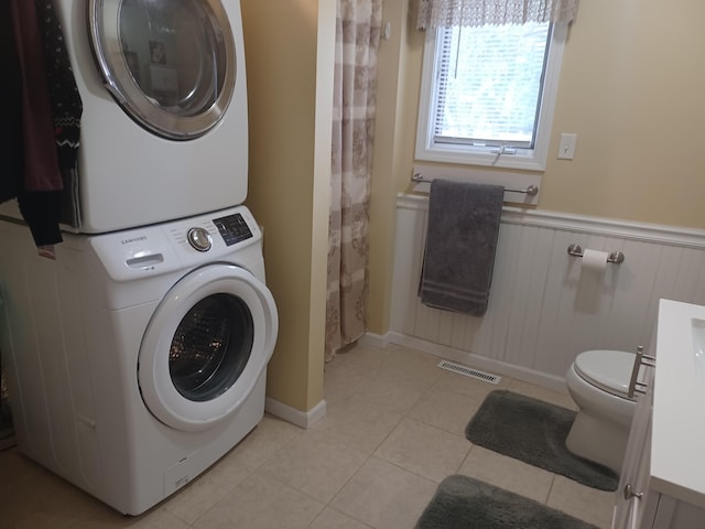 laundry area with stacked washer and dryer, laundry area, visible vents, wainscoting, and light tile patterned flooring