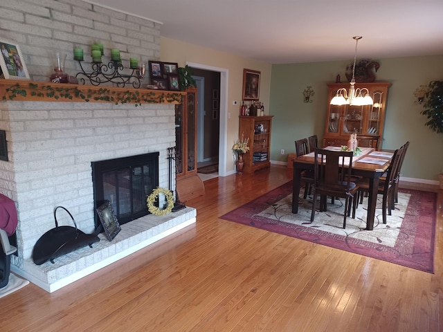 dining space with a chandelier, a fireplace, wood finished floors, and baseboards