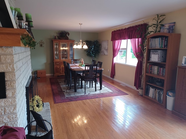 dining area featuring light wood-type flooring, a fireplace, a notable chandelier, and baseboards