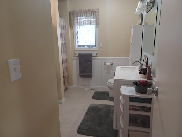 full bathroom with double vanity, toilet, wainscoting, a sink, and tile patterned floors