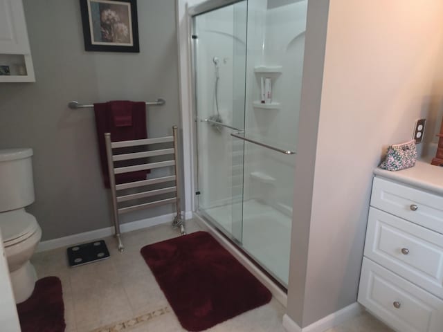 full bath featuring toilet, a shower stall, baseboards, and tile patterned floors