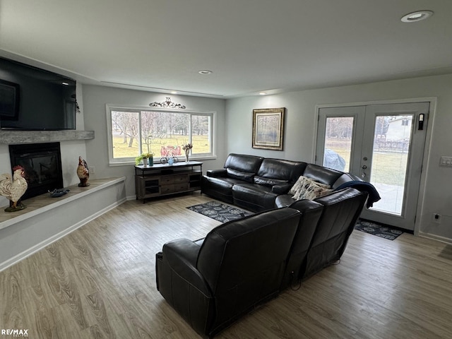 living area featuring french doors, recessed lighting, a glass covered fireplace, wood finished floors, and baseboards