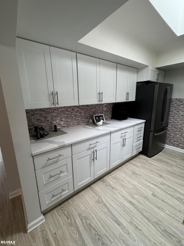 kitchen with light stone counters, backsplash, light wood-style flooring, freestanding refrigerator, and white cabinets