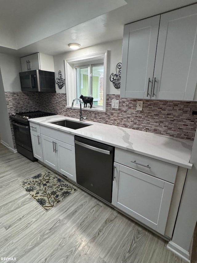 kitchen with decorative backsplash, black range with gas stovetop, light wood-style floors, a sink, and dishwasher