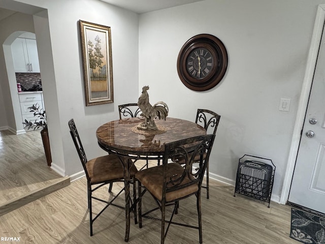 dining room featuring light wood-type flooring, arched walkways, and baseboards