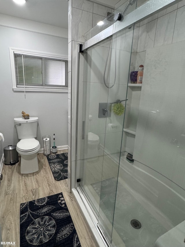 bathroom featuring a stall shower, wood finished floors, toilet, and baseboards