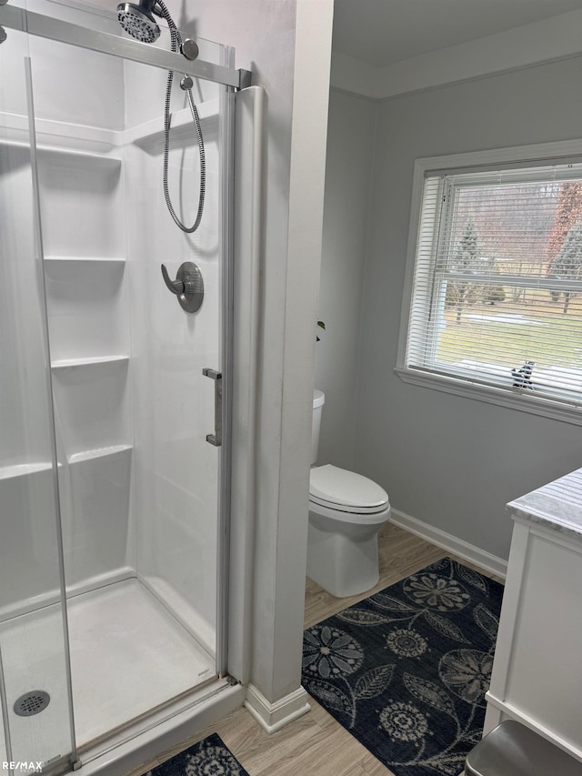 bathroom featuring a stall shower, wood finished floors, toilet, and baseboards