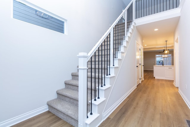 stairs featuring recessed lighting, a towering ceiling, baseboards, and wood finished floors