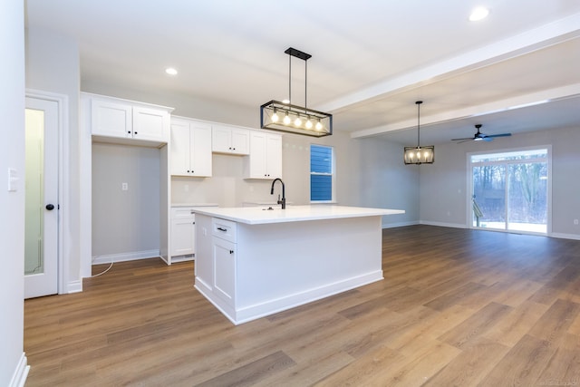 kitchen with light wood-style flooring, a center island with sink, white cabinetry, and baseboards