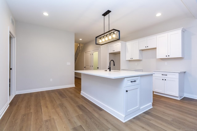 kitchen featuring a center island with sink, baseboards, white cabinets, light wood-style floors, and recessed lighting