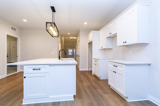 kitchen featuring an island with sink, visible vents, white cabinets, and a sink