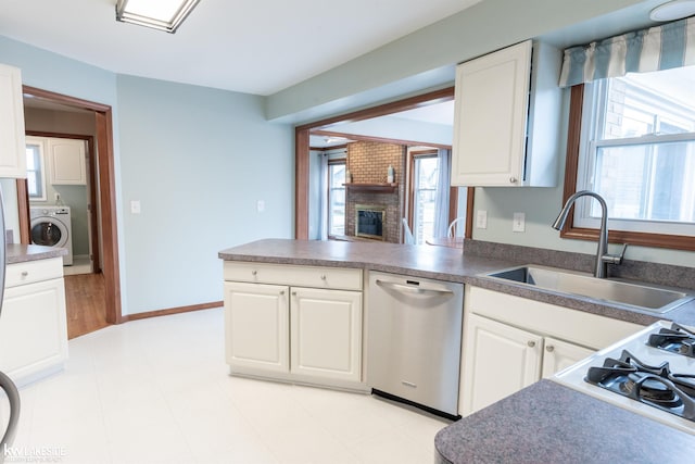 kitchen featuring washer / clothes dryer, stainless steel dishwasher, a fireplace, white cabinetry, and a sink