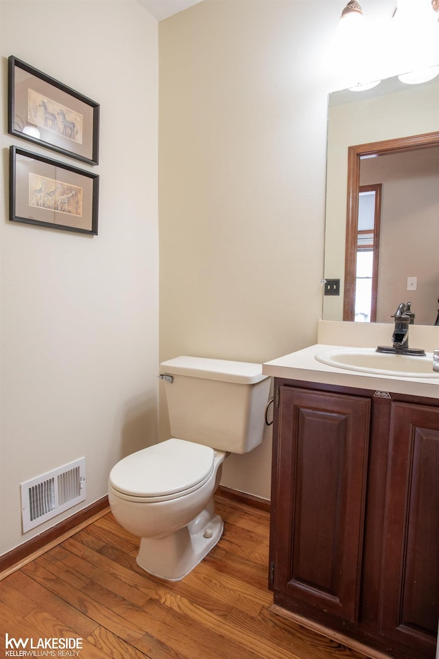 bathroom featuring visible vents, toilet, vanity, wood finished floors, and baseboards