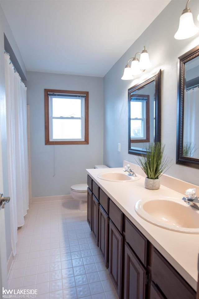 full bathroom with double vanity, a sink, toilet, and baseboards