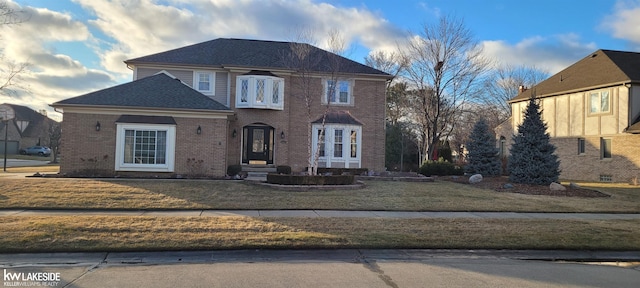 view of front of property with brick siding, a front lawn, and roof with shingles