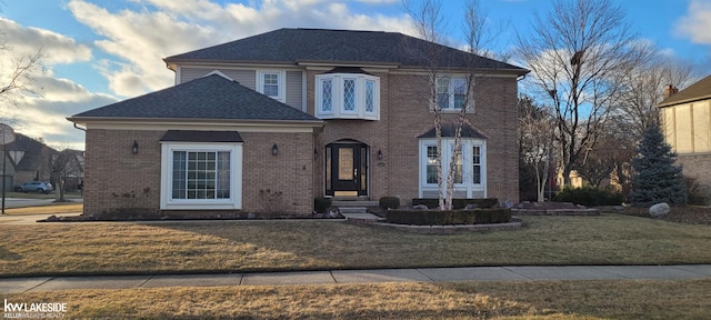 view of front facade with brick siding, a shingled roof, and a front yard