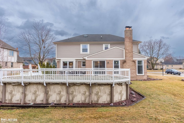 rear view of house with a deck, a yard, brick siding, and a chimney