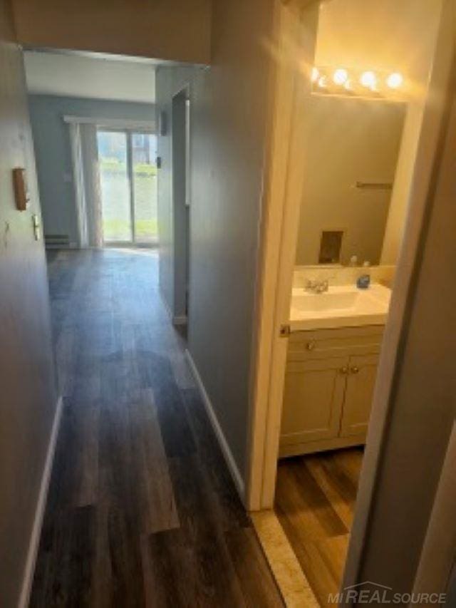 corridor with dark wood-style floors, baseboards, and a sink