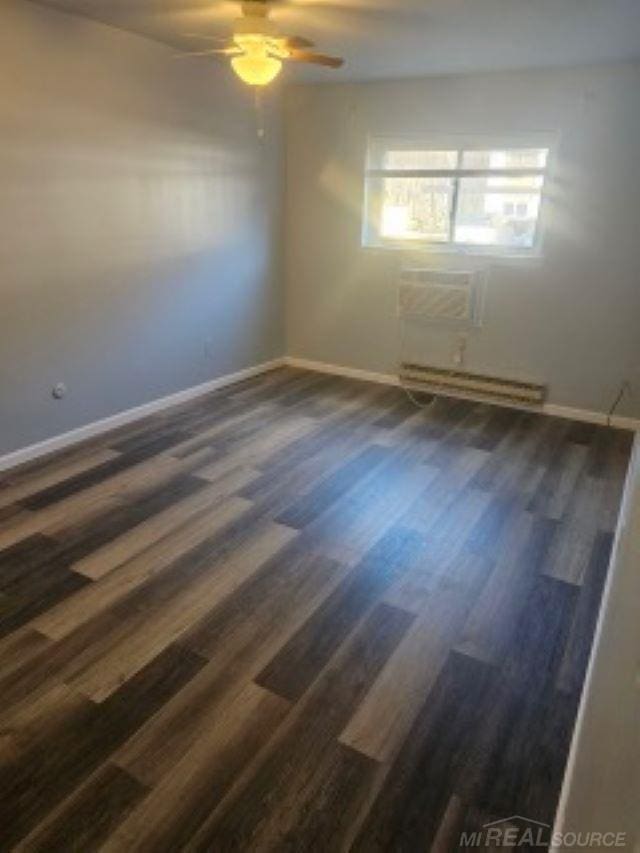 spare room with wood finished floors, a ceiling fan, baseboards, an AC wall unit, and baseboard heating