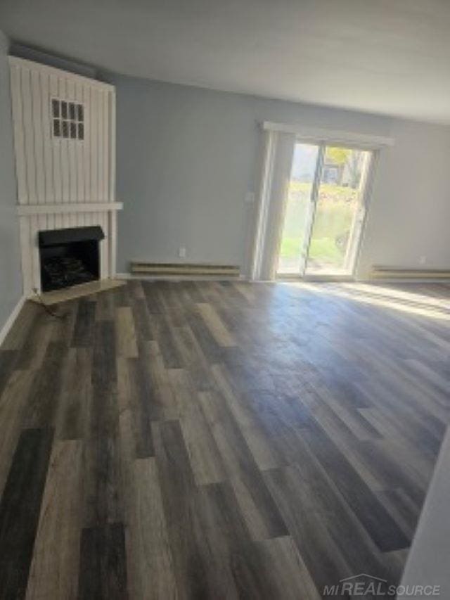 unfurnished living room with a large fireplace, a baseboard heating unit, and dark wood finished floors