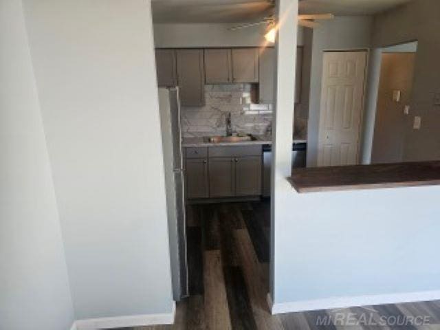 kitchen featuring baseboards, decorative backsplash, dark wood finished floors, freestanding refrigerator, and a sink