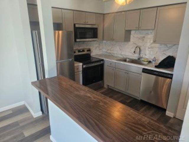 kitchen featuring dark wood finished floors, stainless steel appliances, decorative backsplash, gray cabinetry, and a sink