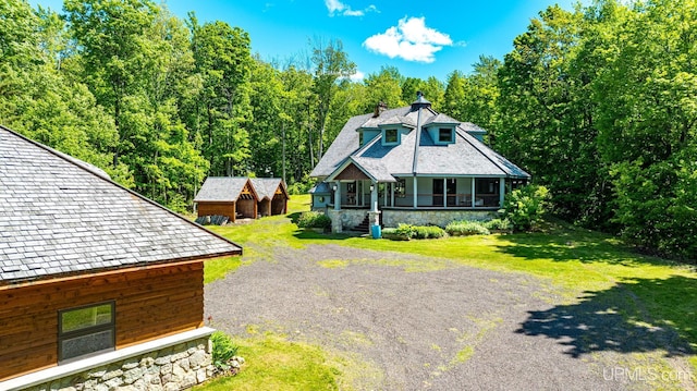 view of front of property featuring a porch, an outdoor structure, stone siding, driveway, and a front yard