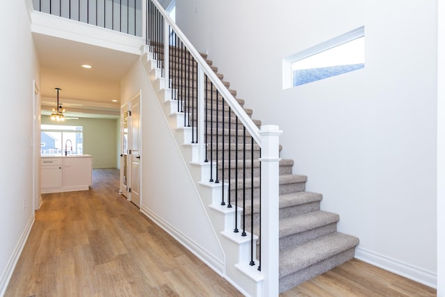 stairs with a high ceiling, recessed lighting, wood finished floors, and baseboards