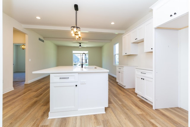 kitchen featuring visible vents, white cabinets, an island with sink, light wood-style flooring, and a sink