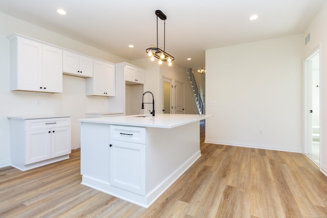 kitchen featuring an island with sink, a sink, visible vents, and white cabinets