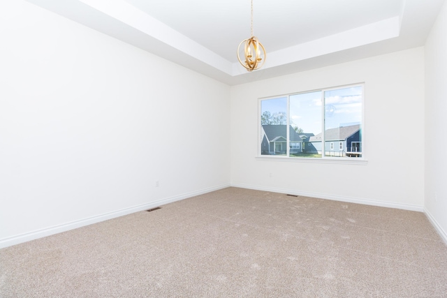 empty room featuring a chandelier, a raised ceiling, carpet floors, and baseboards