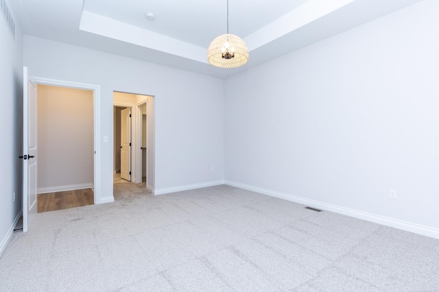 unfurnished room with carpet floors, baseboards, a raised ceiling, and a notable chandelier