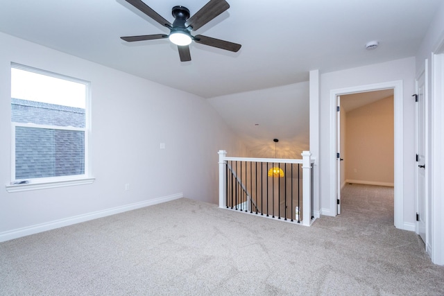 carpeted empty room featuring a ceiling fan, vaulted ceiling, and baseboards